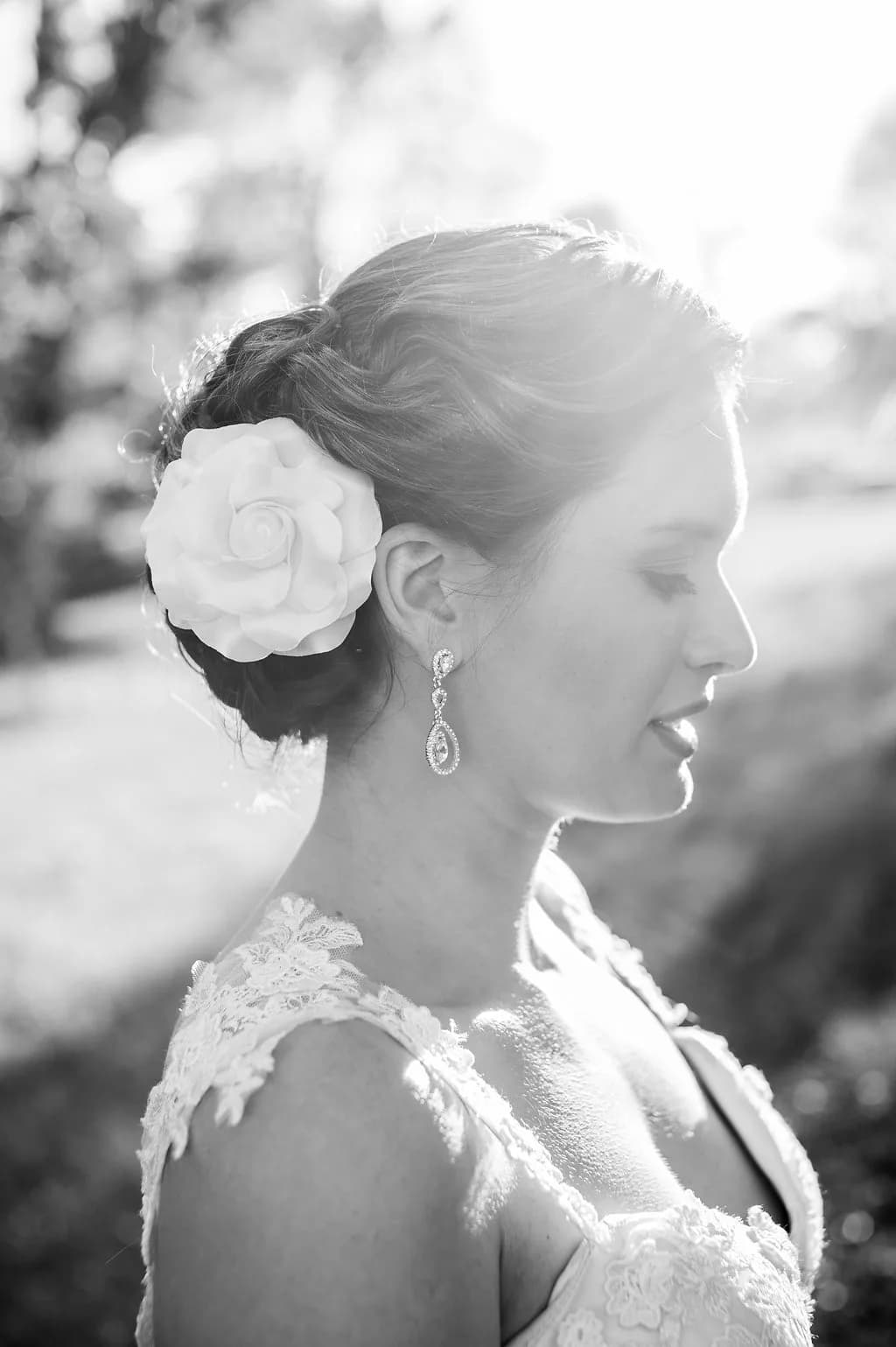 Black and white bridal portrait with floral hair accessory and chandelier earrings, soft backlit outdoor setting