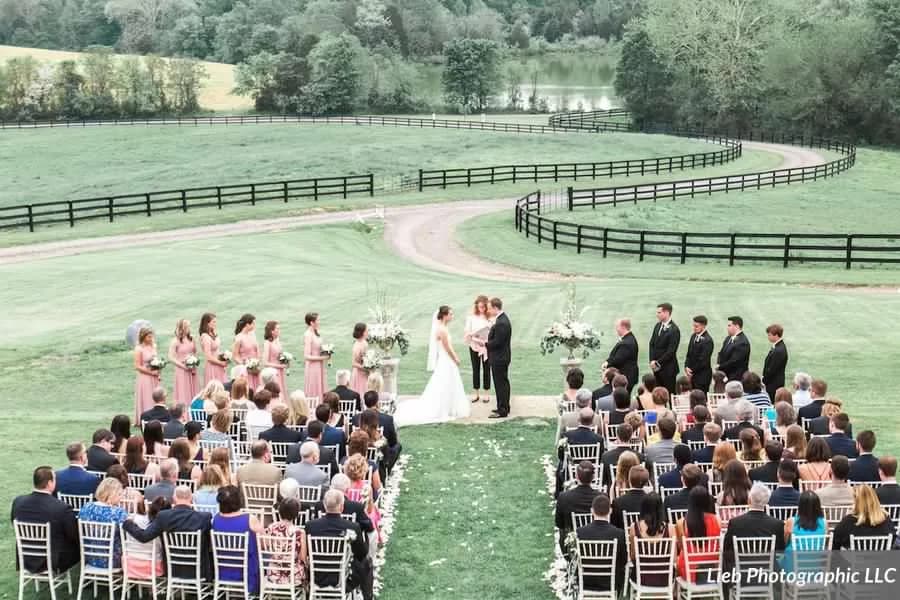 Outdoor wedding ceremony at Rixey Manor with bride and groom at altar, guests seated in rows on manicured lawn with black fencing
