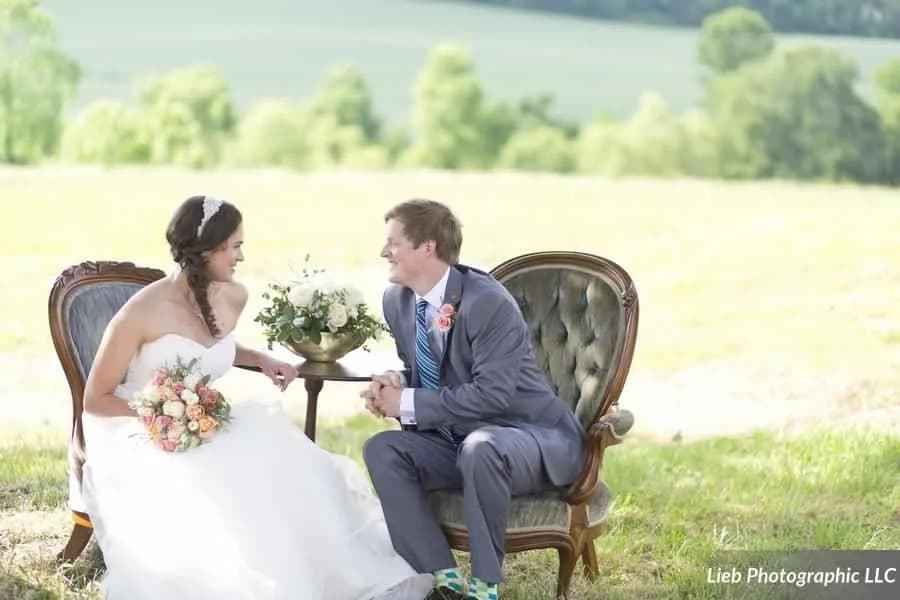 Bride and groom laughing together on a tufted vintage settee on the sun-drenched Virginia countryside grounds
