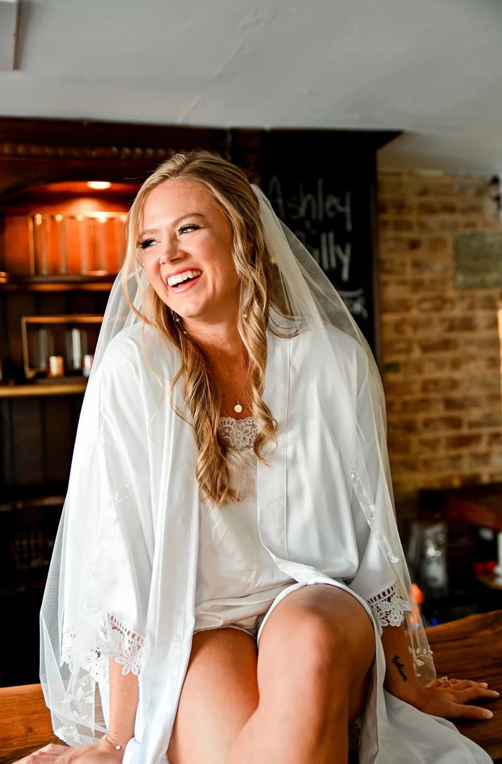 Bride in white lace dress and veil smiling during getting-ready session in modern interior
