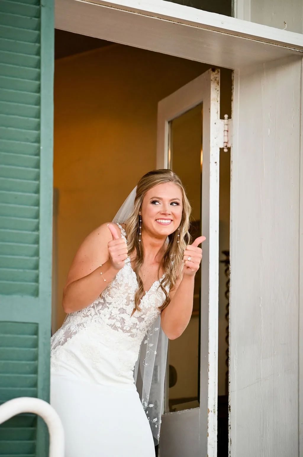 Bride in white wedding dress with veil smiling at doorway during getting-ready preparations