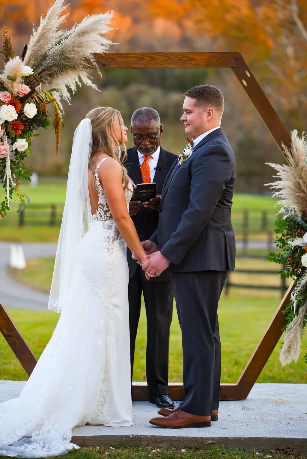 Bride and groom hold hands at outdoor hexagonal arch ceremony at Rixey Manor amid vibrant fall foliage