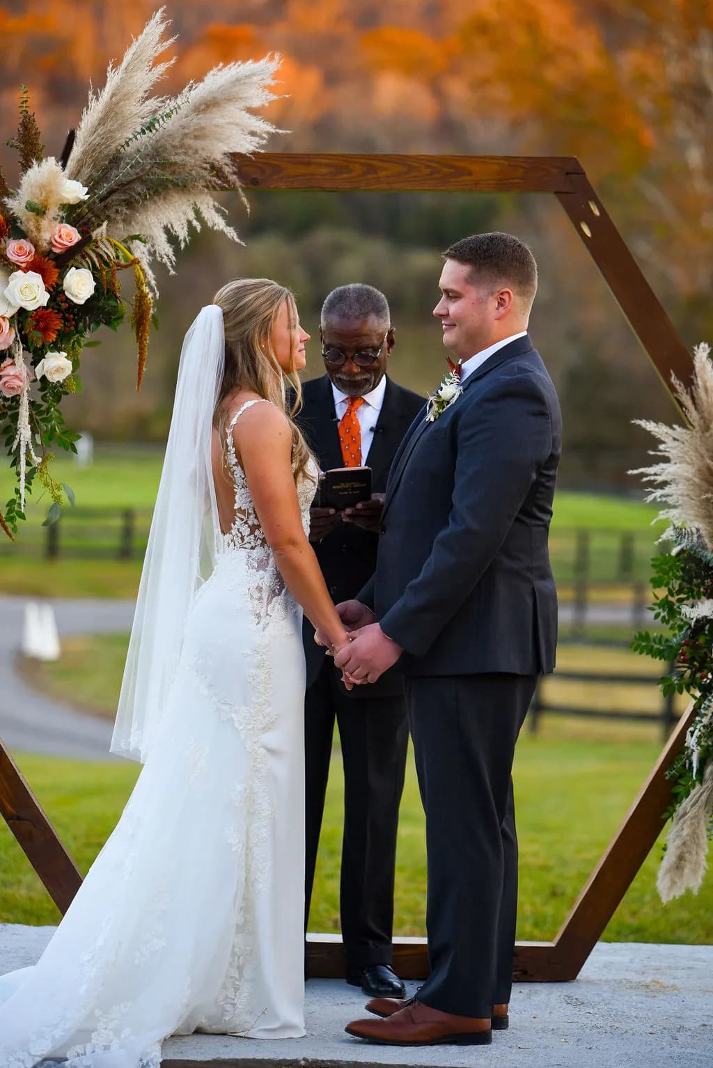 Bride and groom exchange vows under floral hexagon arch at Rixey Manor with vibrant autumn foliage backdrop