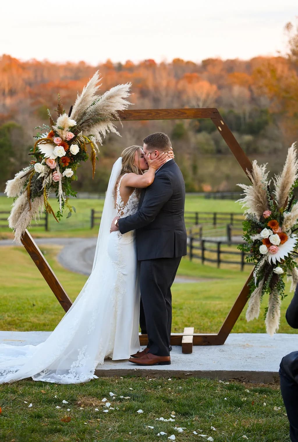 Bride and groom share first kiss under hexagonal wooden arch with fall florals at Rixey Manor outdoor ceremony
