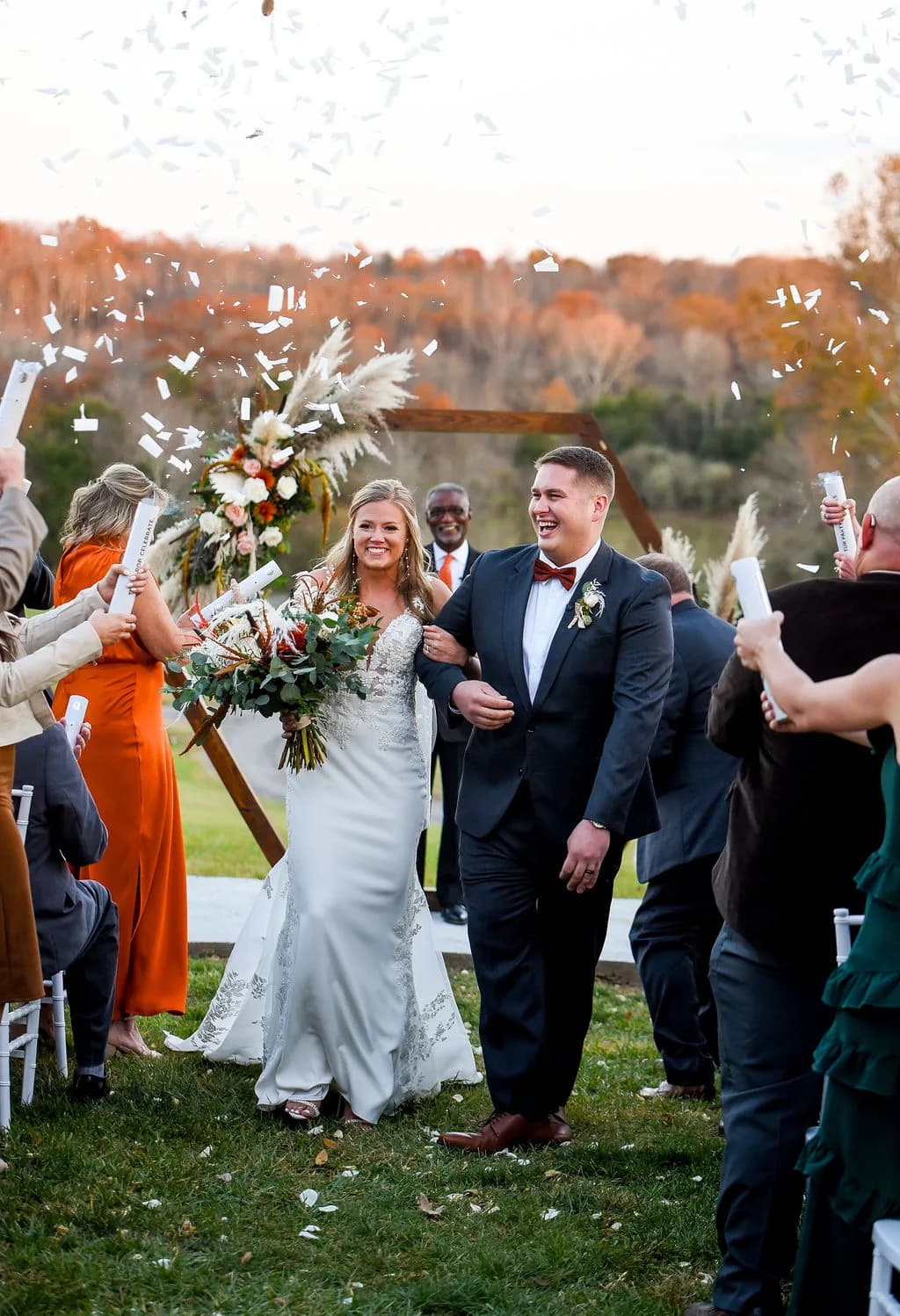 Bride and groom walk back up the aisle through confetti at an outdoor fall ceremony at Rixey Manor