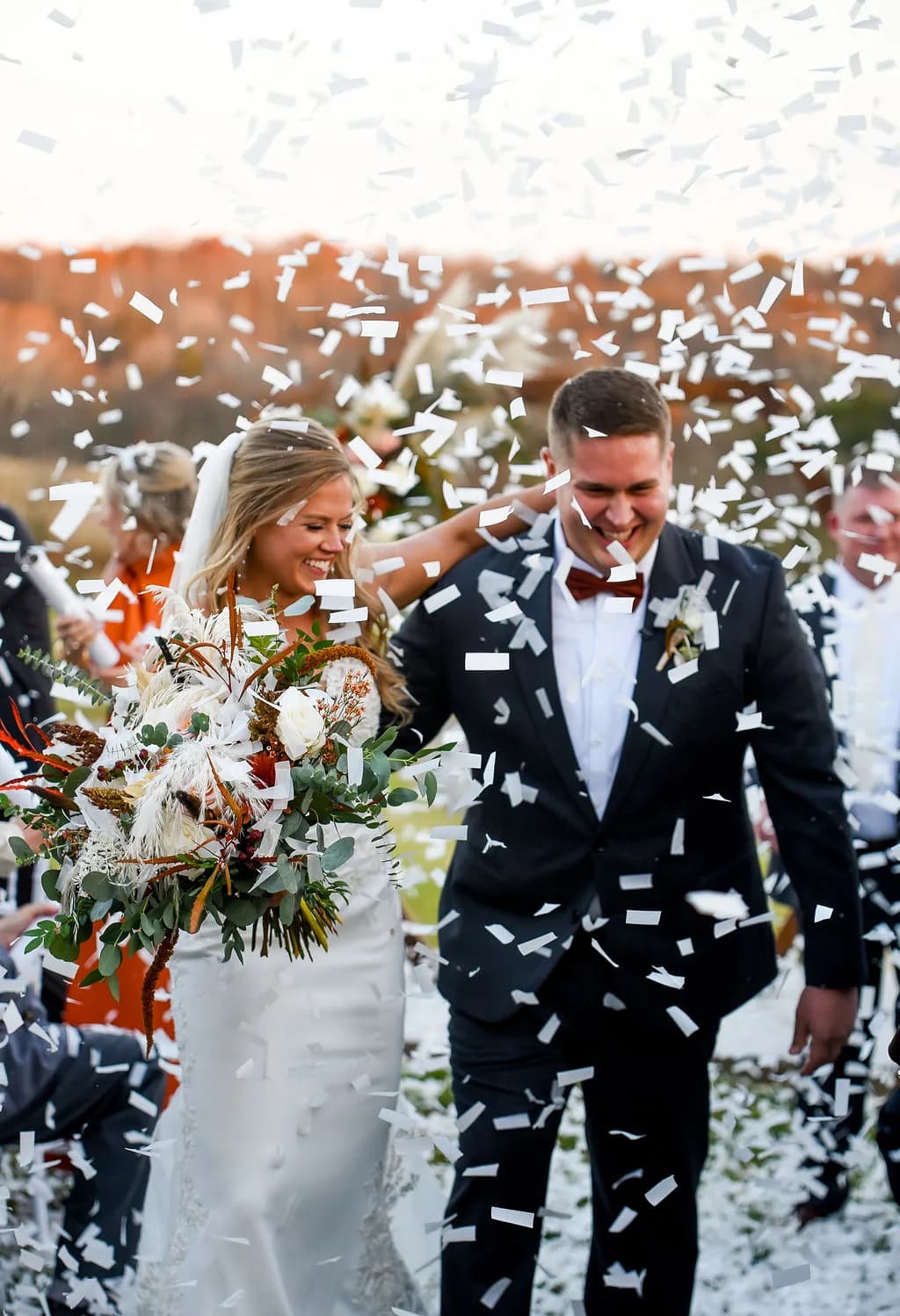 Bride and groom walking through confetti shower at outdoor reception with manor in background