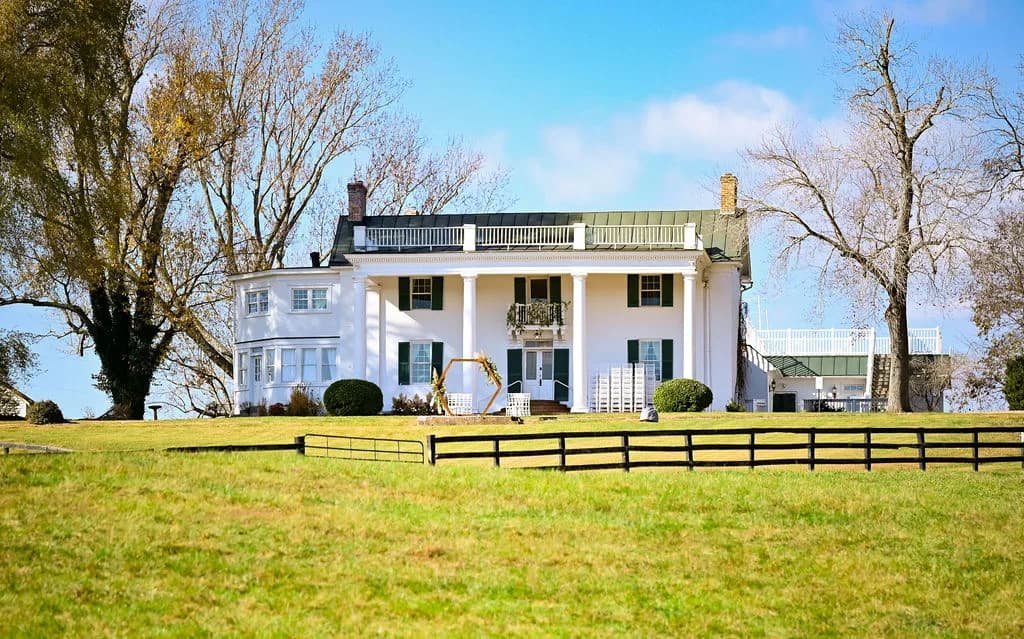 Rixey Manor estate exterior with white columns, green roof, wooden fence, and lush grounds on a clear day
