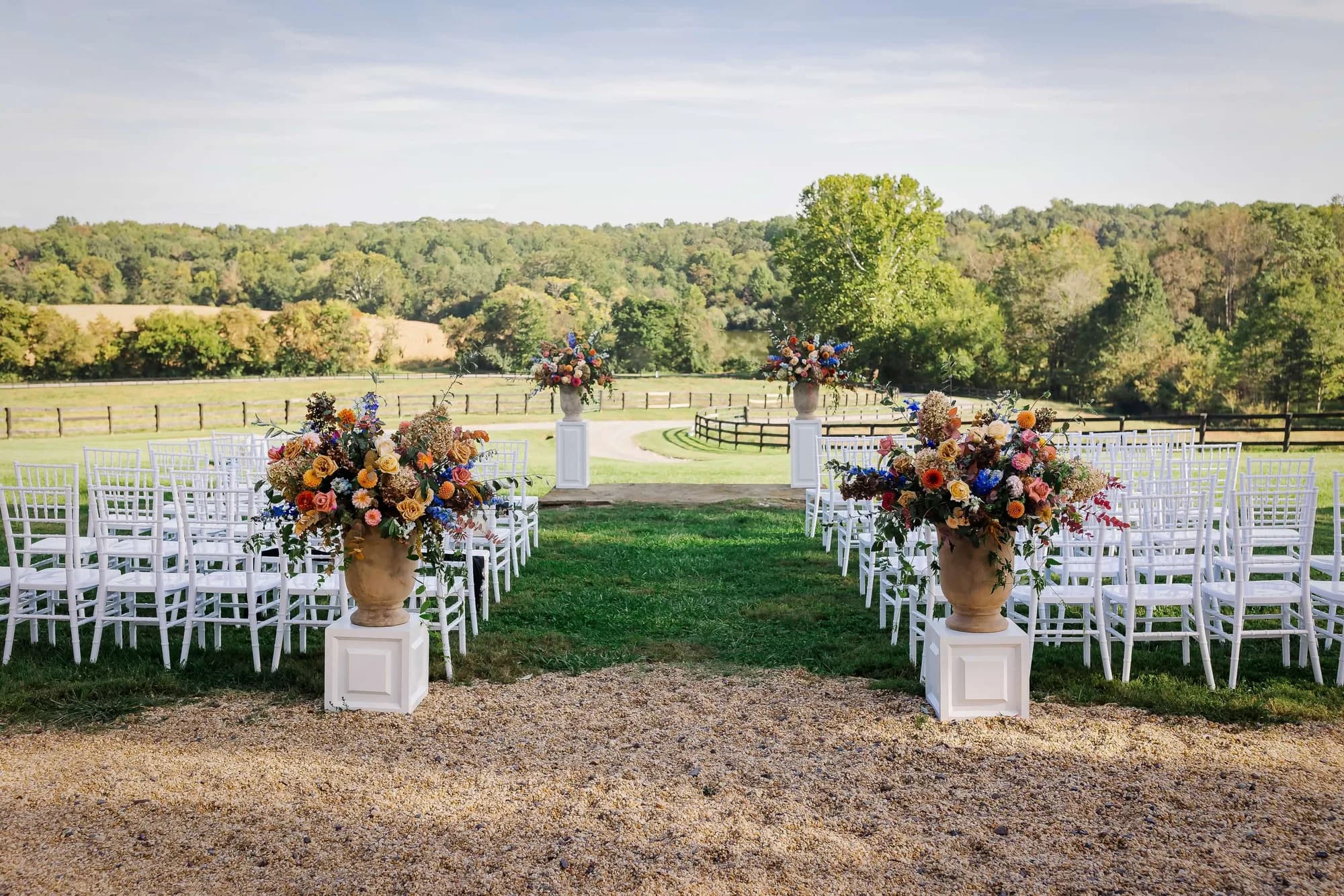 Outdoor ceremony aisle at Rixey Manor with colorful floral urns, white chairs, and sweeping Virginia countryside views