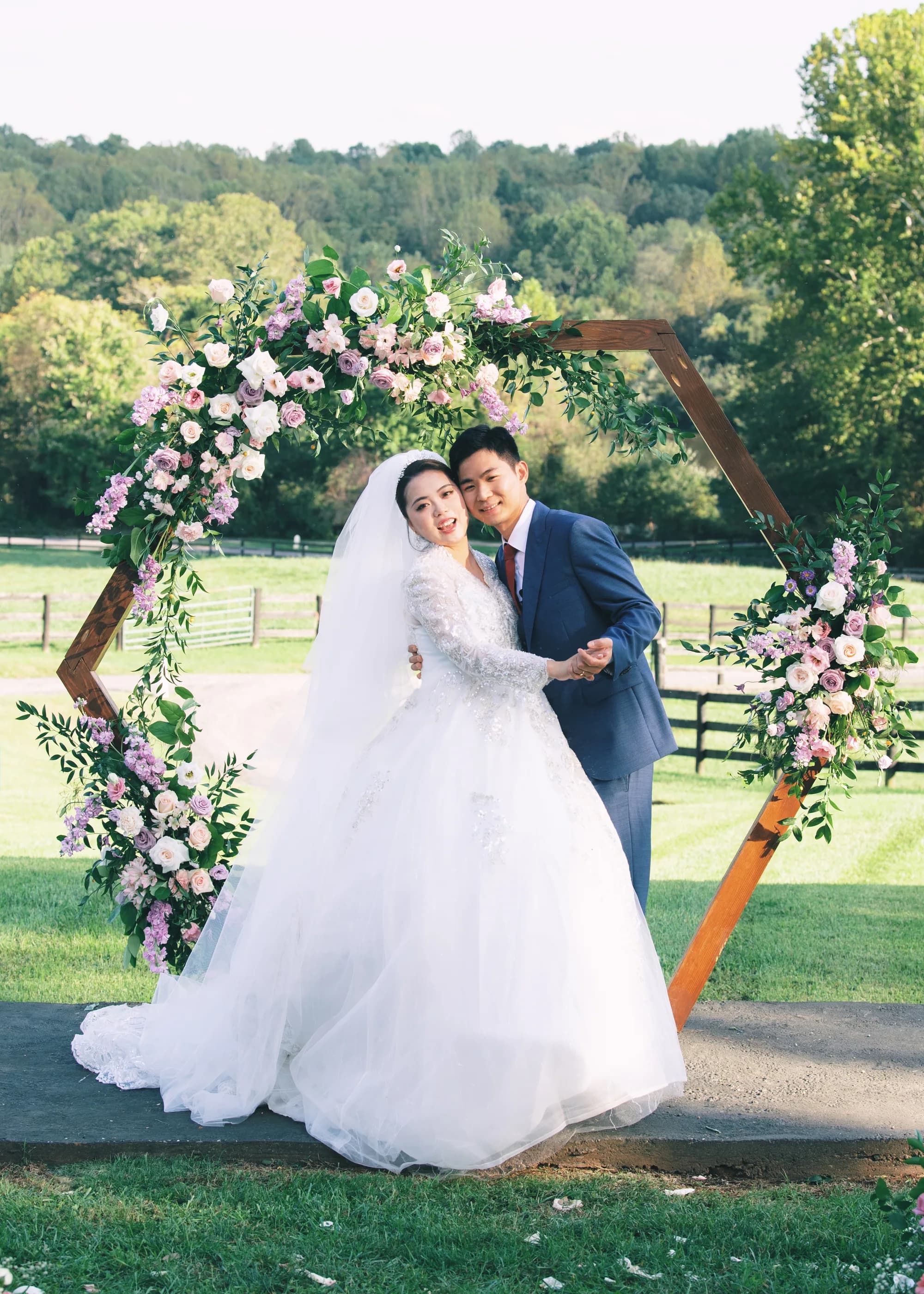 Bride and groom portrait under floral hexagon arch on Rixey Manor's sunlit green lawn