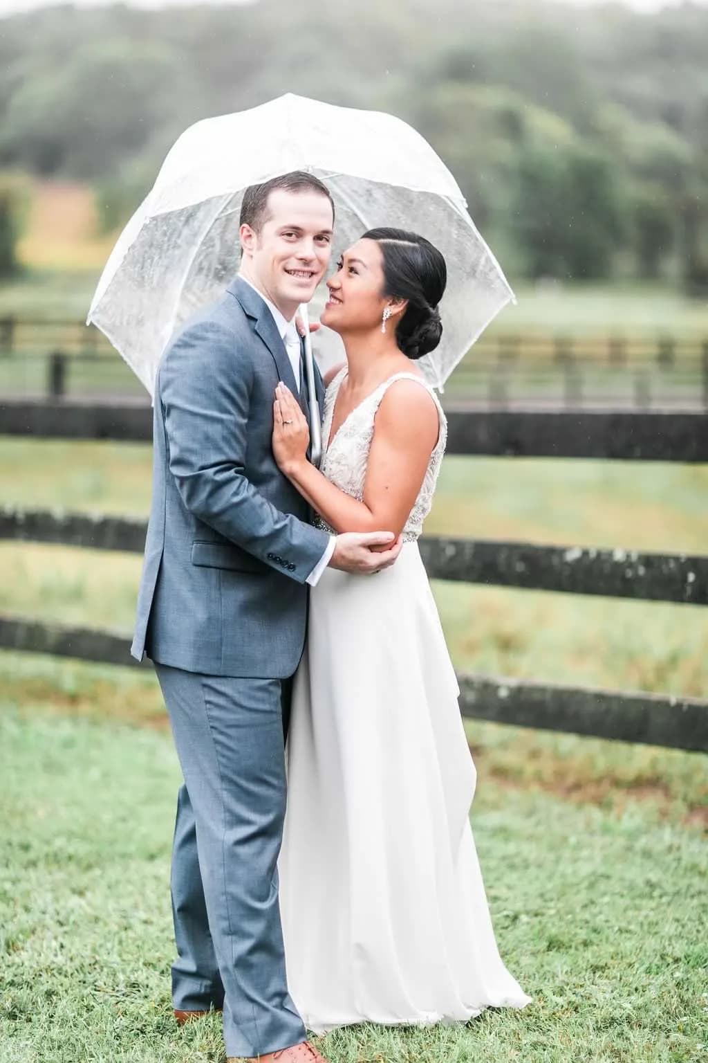 Bride and groom embrace under a clear umbrella in the rain on Rixey Manor's lush grounds