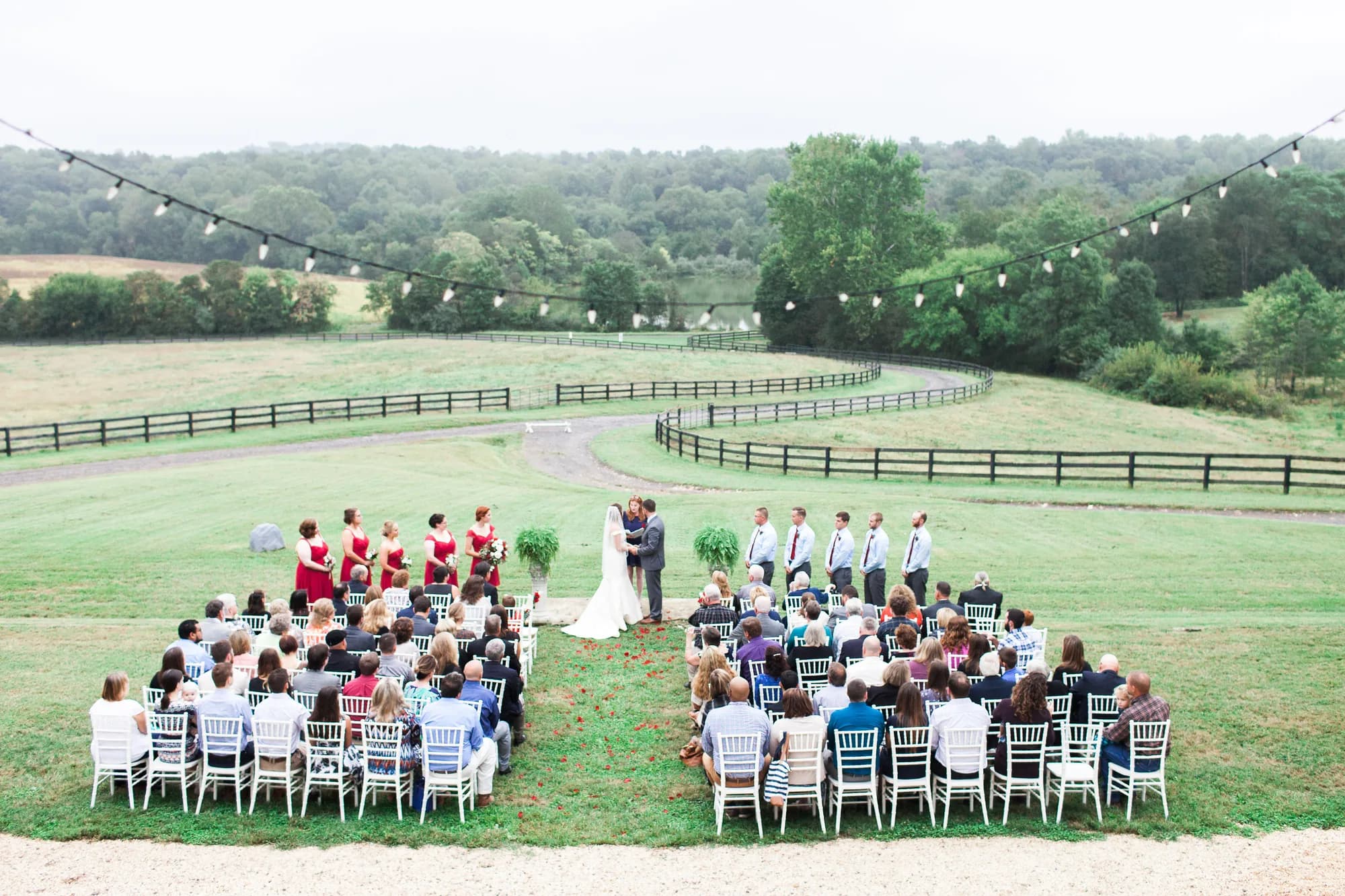 Aerial view of outdoor wedding ceremony on Rixey Manor's rolling Virginia hillside with string lights and full bridal party