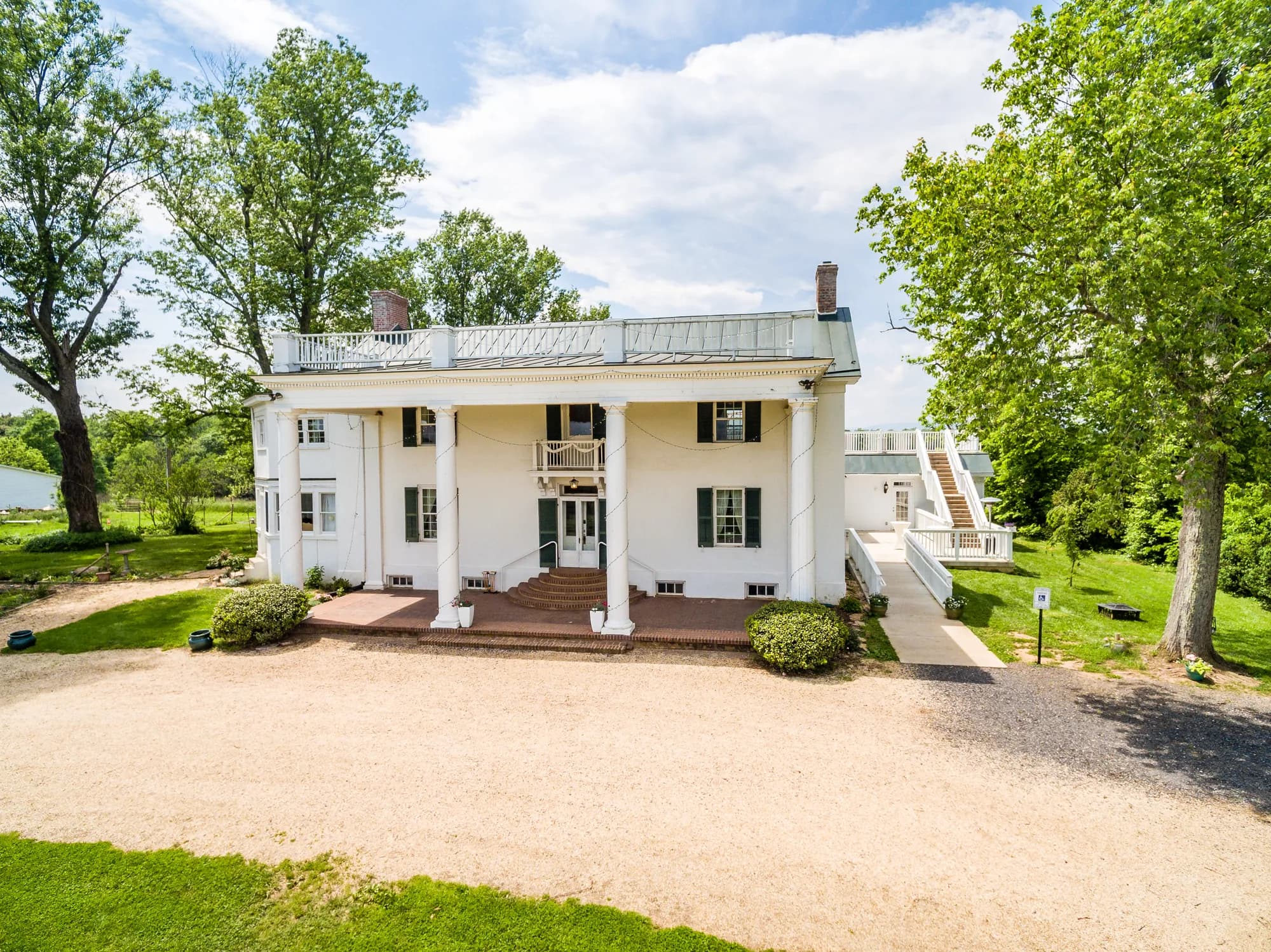 Aerial view of Rixey Manor's white columned facade, rooftop terrace, and tree-lined grounds on a sunny day