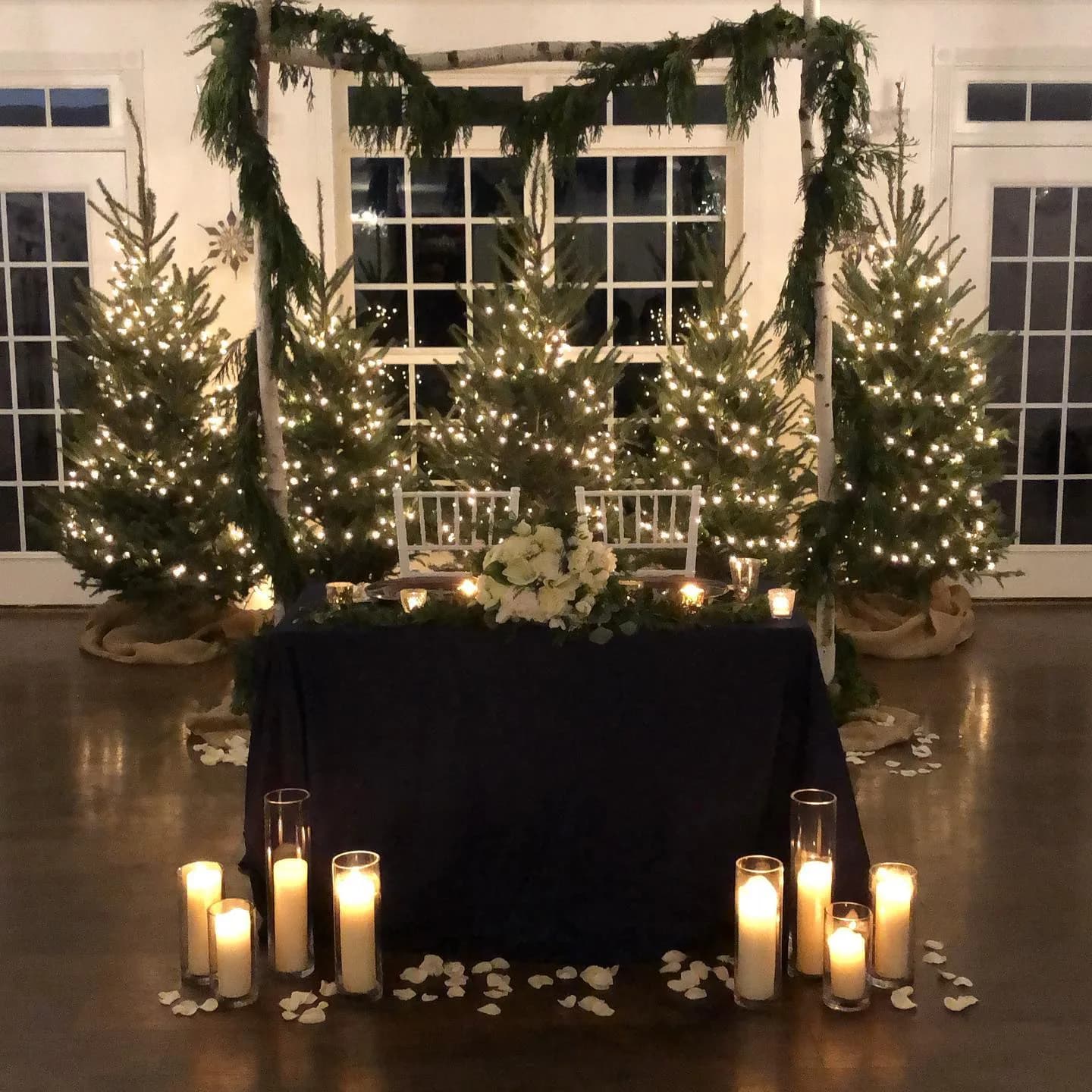 Candlelit sweetheart table flanked by lit Christmas trees and garland arch at Rixey Manor winter wedding reception