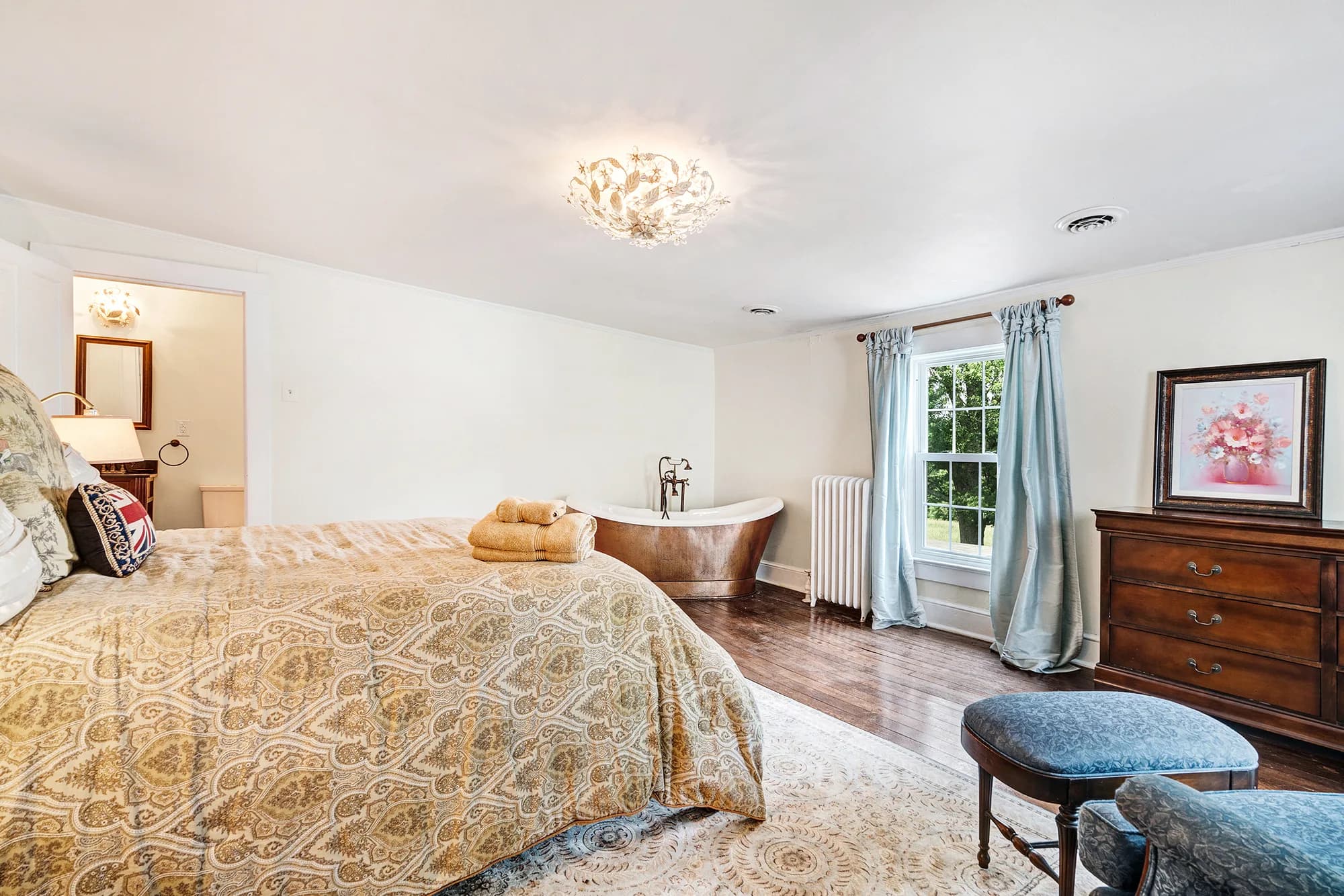 Elegant master suite at Rixey Manor with copper soaking tub, hardwood floors, and light blue drapes