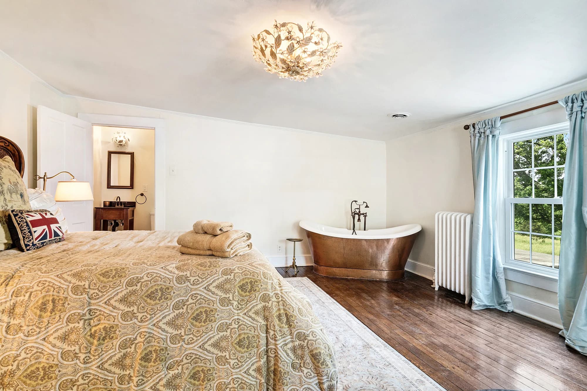 Luxurious bedroom suite with copper soaking tub, ornate ceiling light, and garden views at Rixey Manor