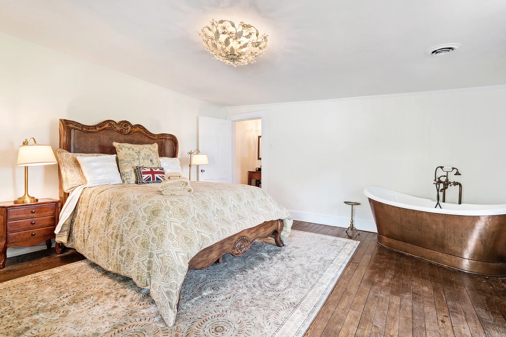 Elegant bedroom suite at Rixey Manor with ornate bed, copper soaking tub, and warm hardwood floors