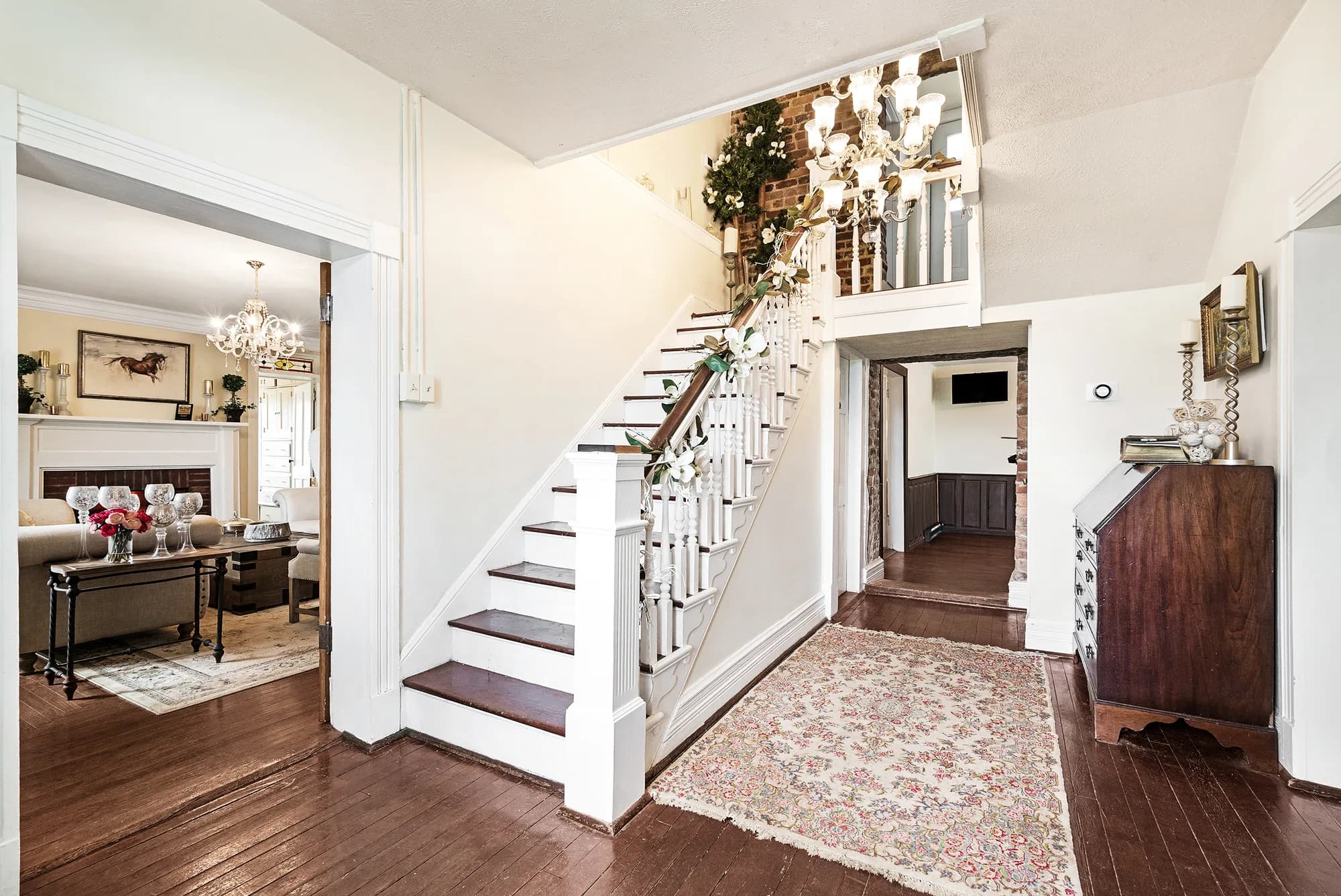 Grand staircase foyer at Rixey Manor with dark hardwood floors, white balustrades, and chandelier above.