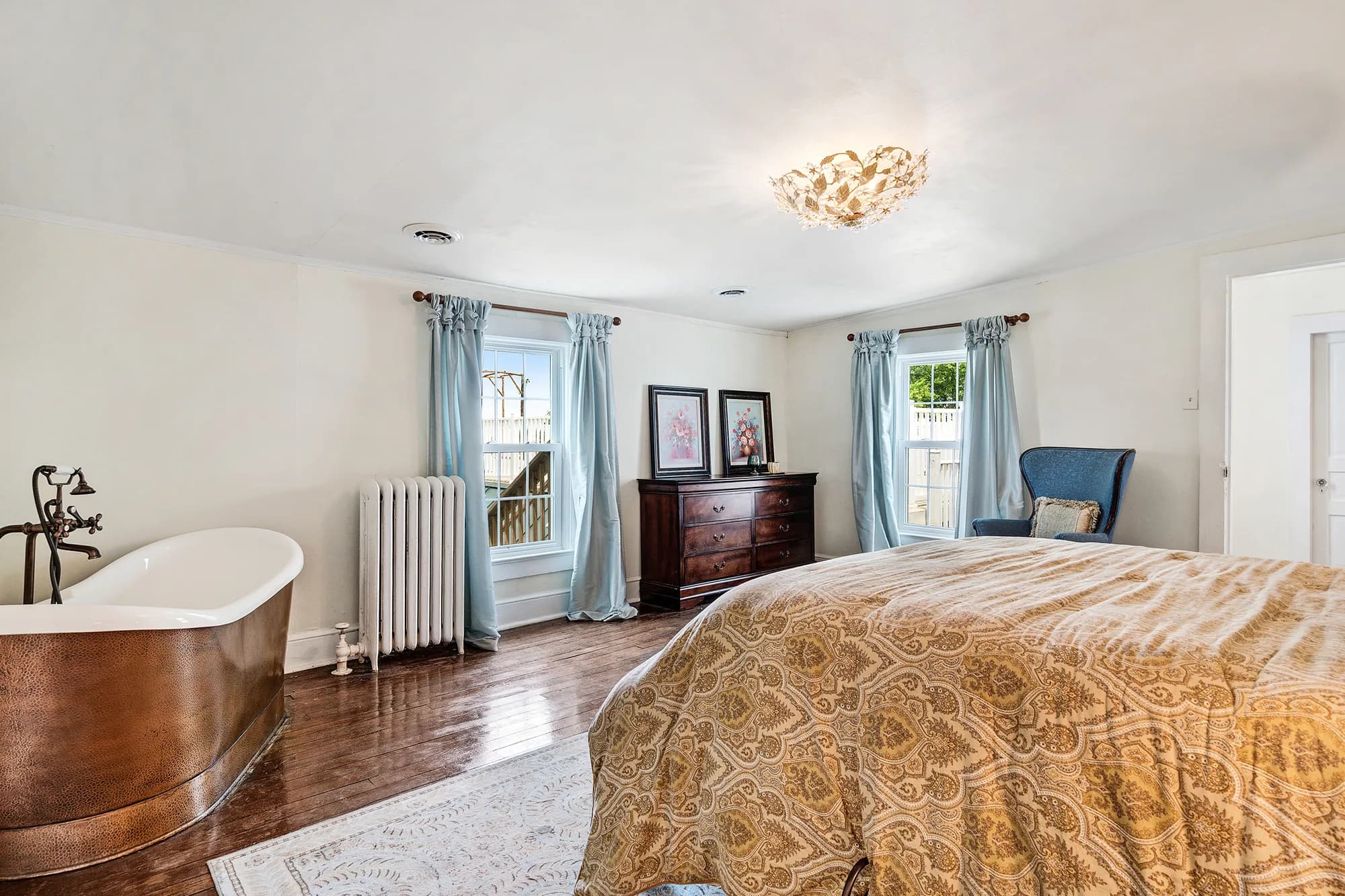 Sunlit master suite at Rixey Manor with copper soaking tub, hardwood floors, and elegant gold bedding