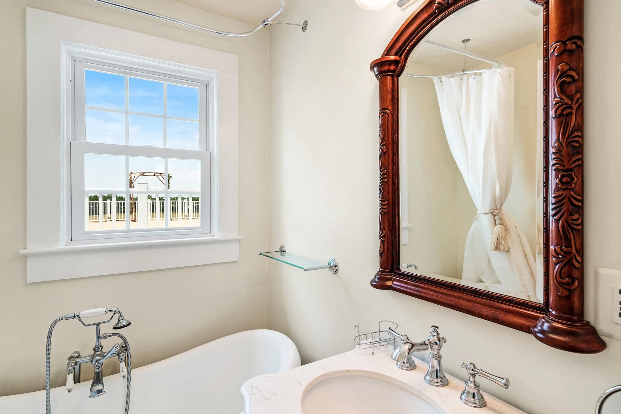 Elegant bathroom at Rixey Manor with ornate mahogany mirror, clawfoot tub, and window overlooking estate grounds