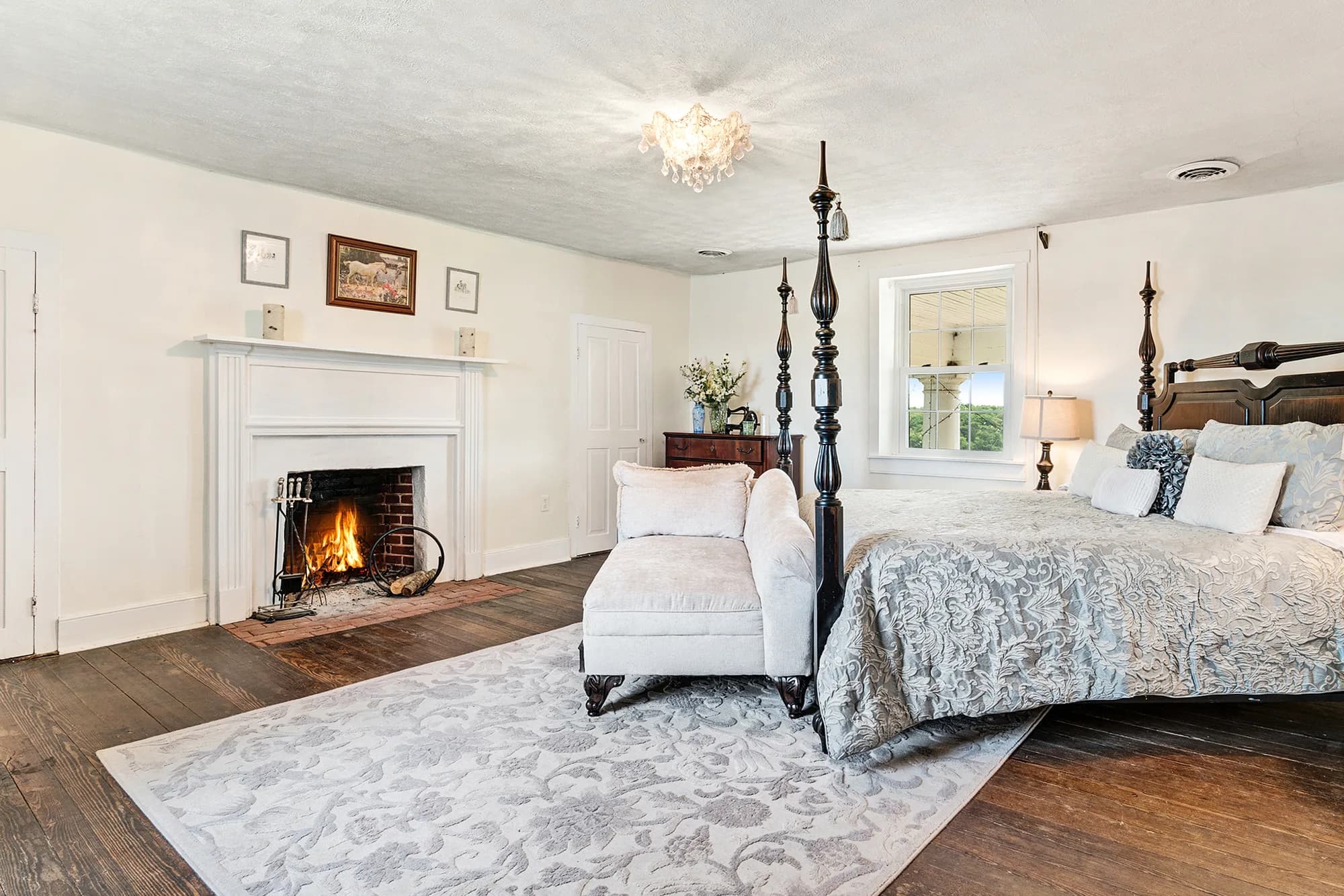 Elegant master bedroom at Rixey Manor with four-poster bed, lit fireplace, hardwood floors, and chandelier
