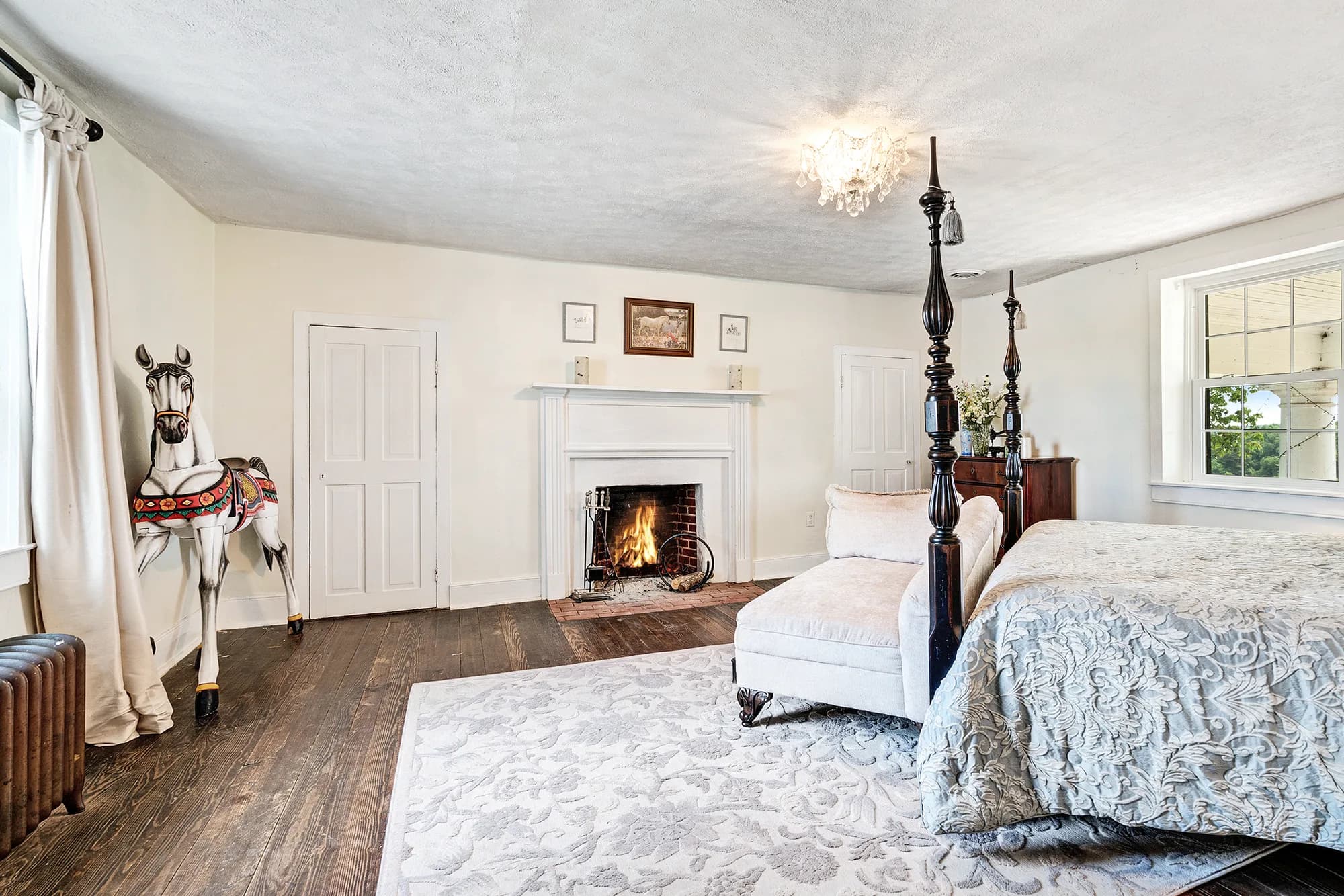 Elegant historic bedroom with lit fireplace, four-poster bed, and decorative carousel horse at Rixey Manor