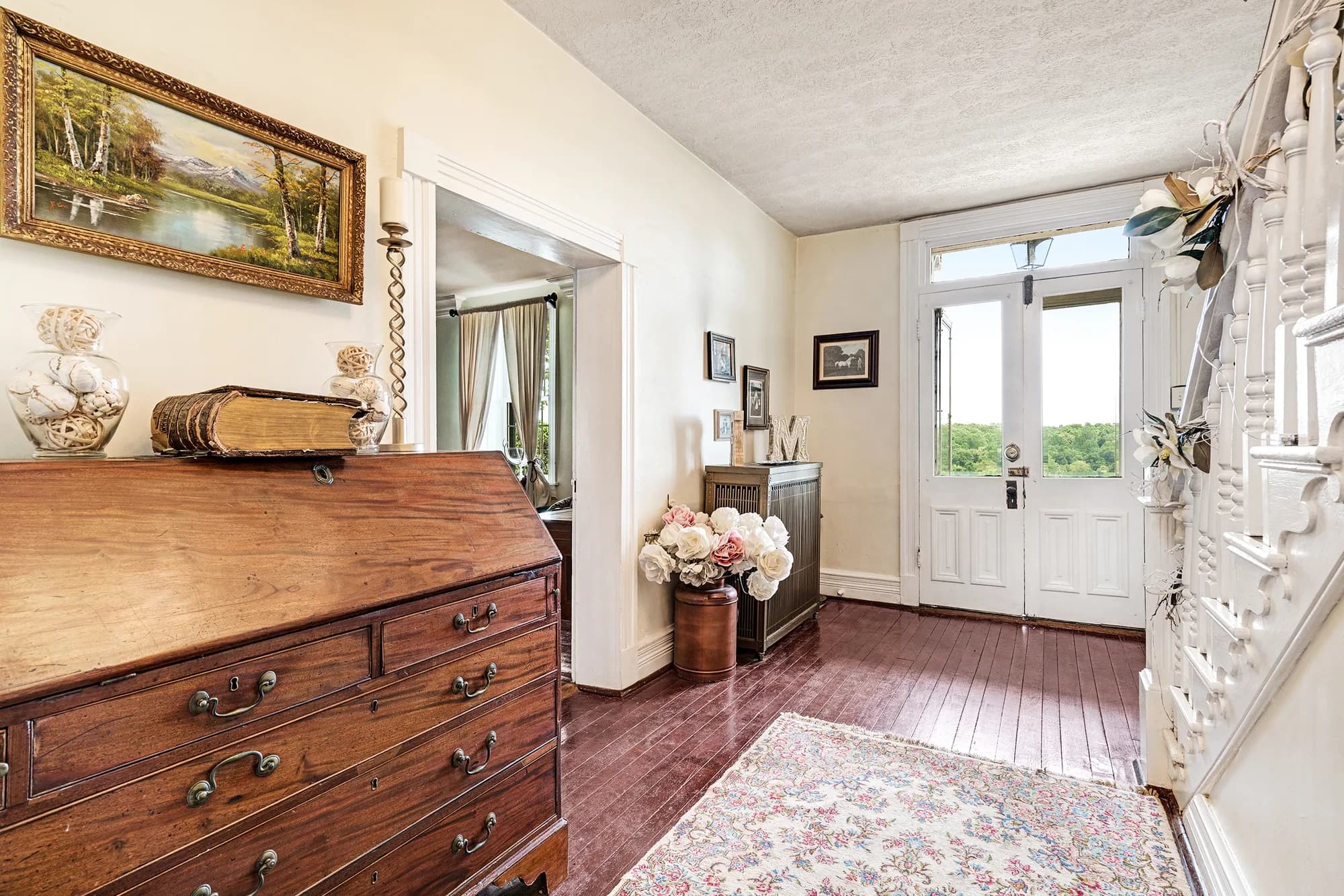 Elegant foyer with wooden dresser, floral arrangement, and doors opening to grounds at Rixey Manor.