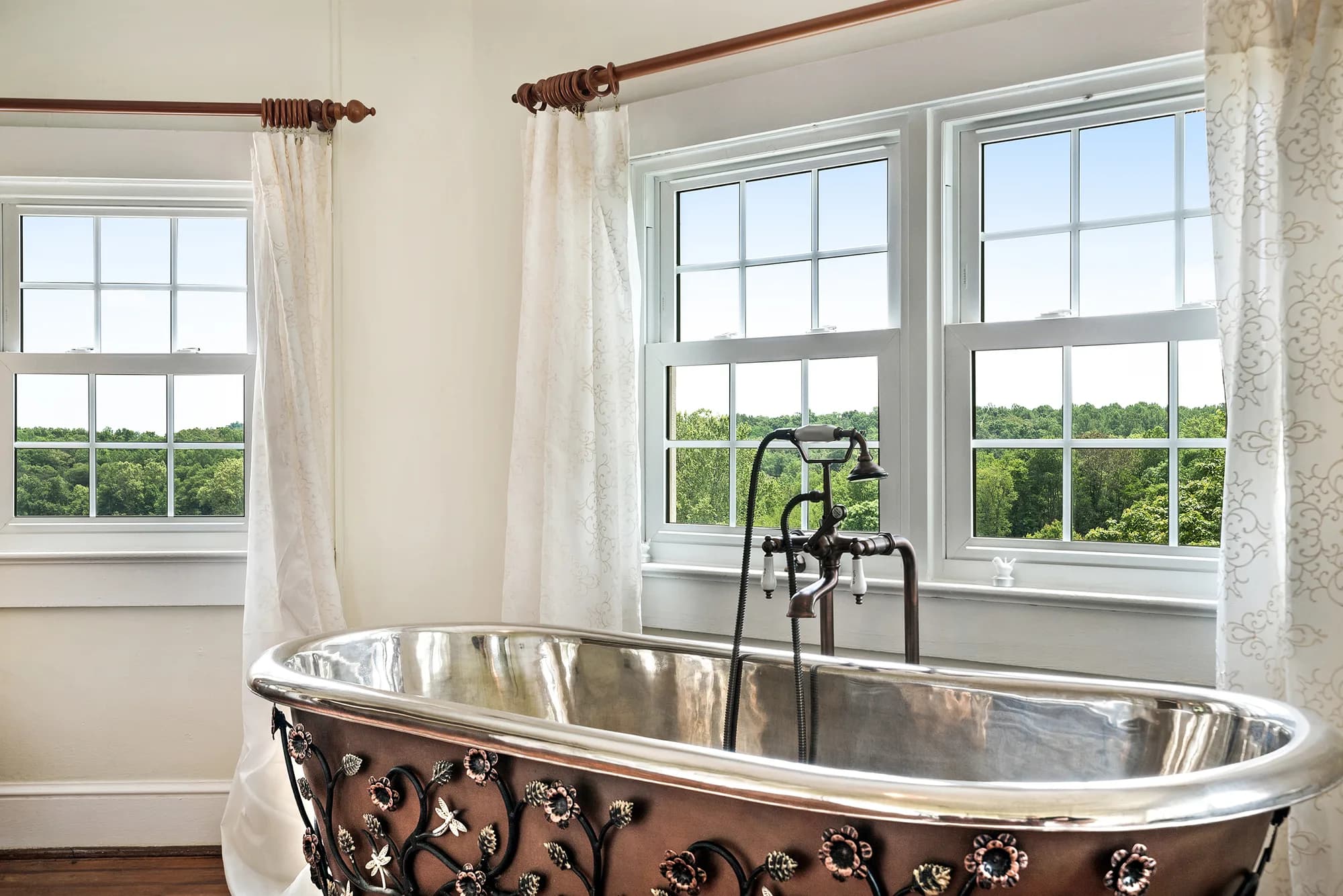 Ornate copper and iron freestanding bathtub beside sunlit windows overlooking Virginia treetops at Rixey Manor