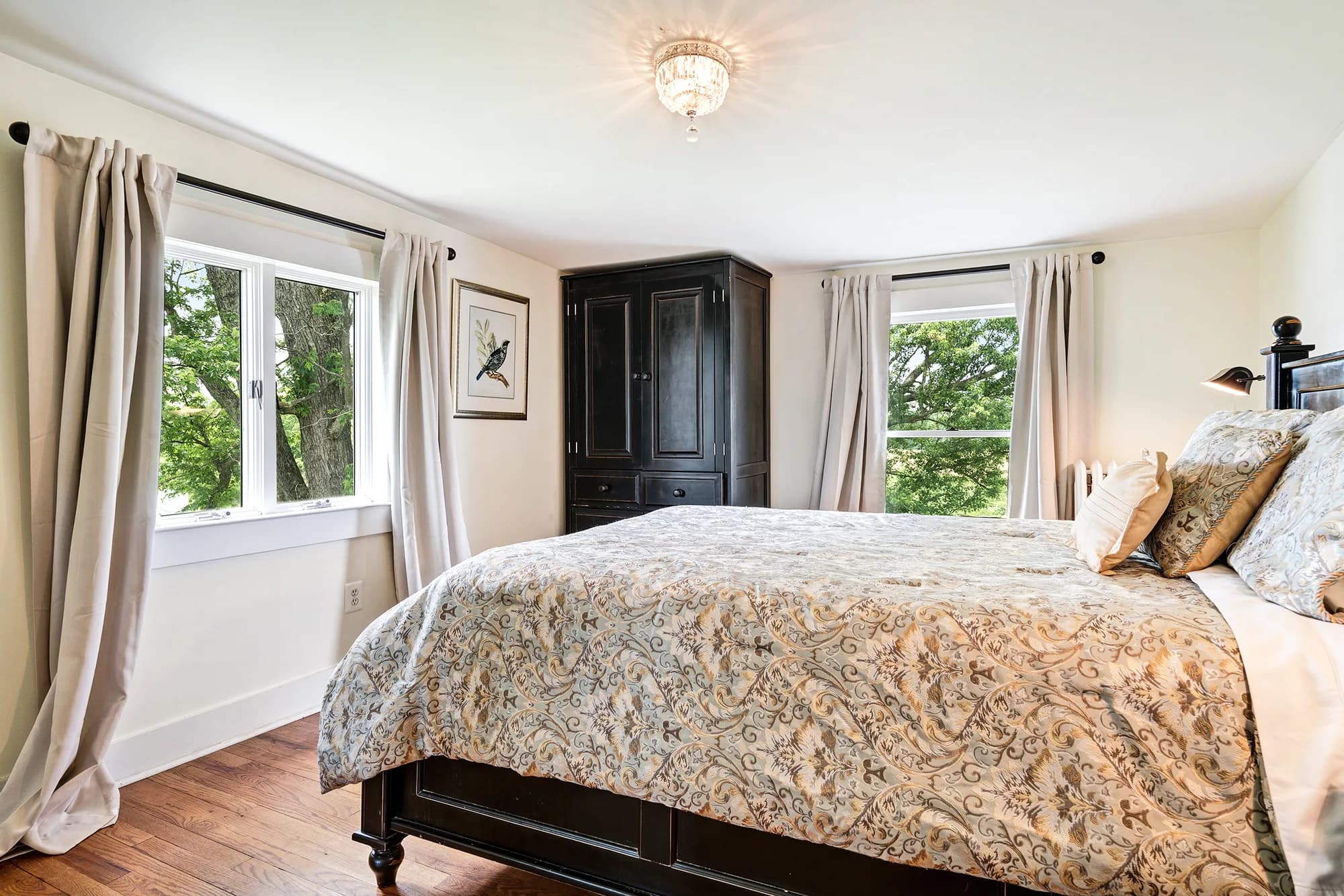 Bright guest bedroom at Rixey Manor with dark wood furniture, floral bedding, and tree-lined windows