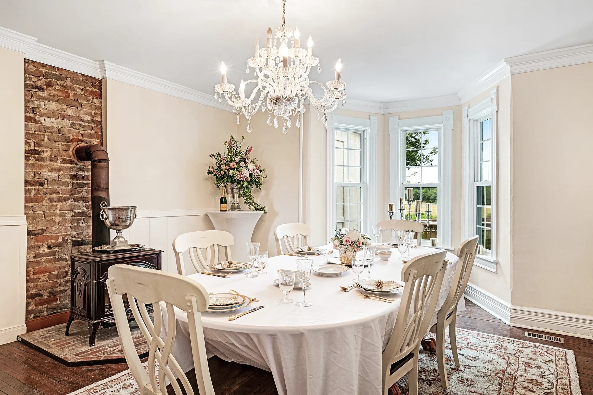 Elegant dining room at Rixey Manor with crystal chandelier, set table, exposed brick fireplace, and bay windows