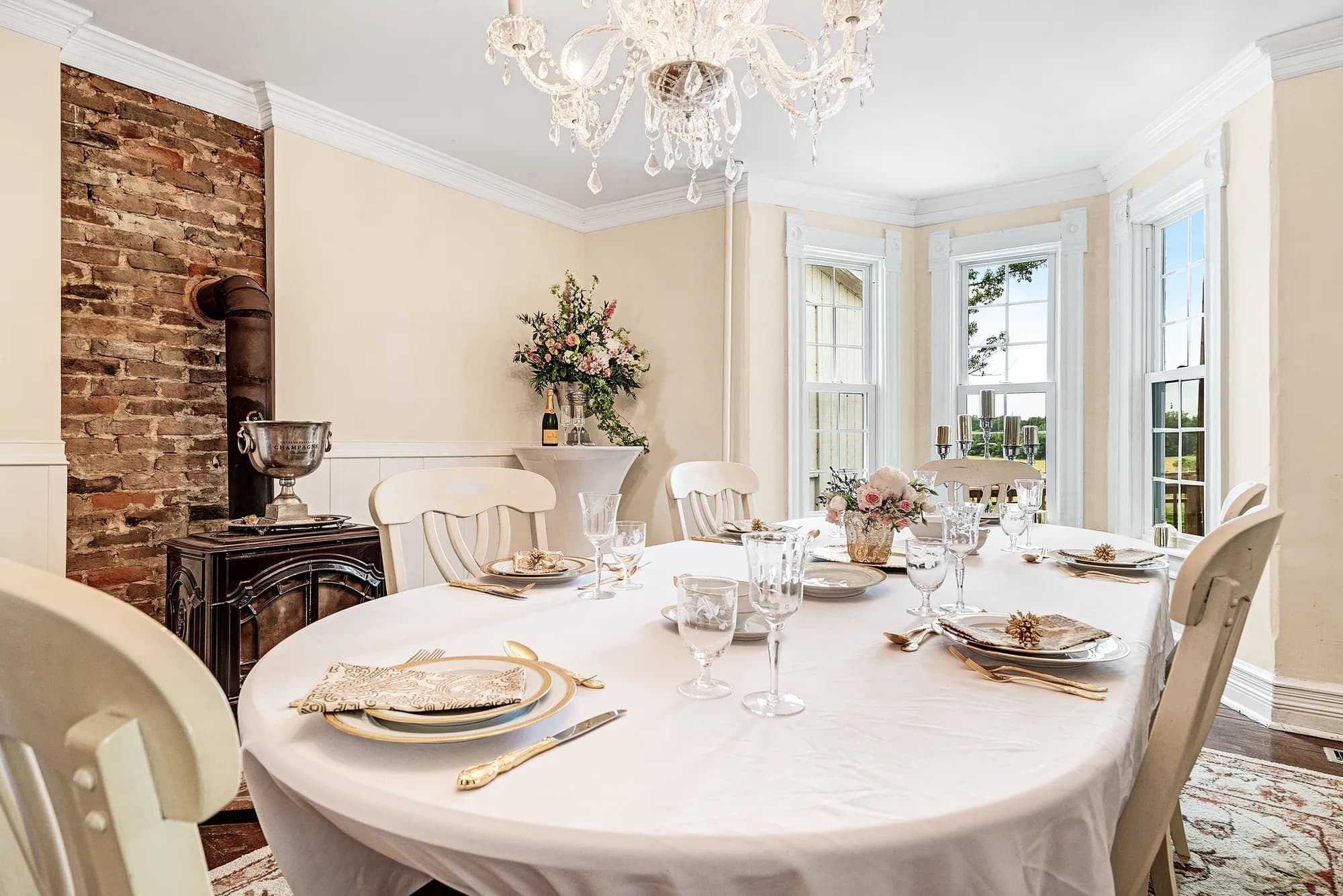 Elegant formal dining room with round table, place settings, chandelier, fireplace, and garden views