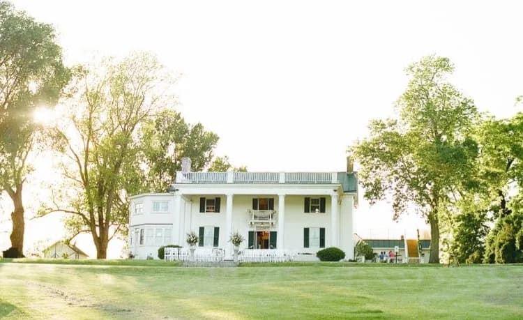 Rixey Manor white columned estate glowing in golden hour light surrounded by mature trees and manicured lawn